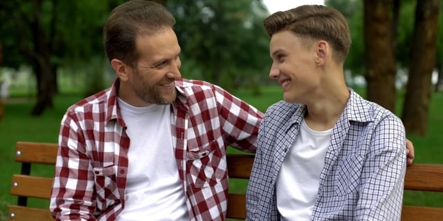 father son talking sitting on bench in park
