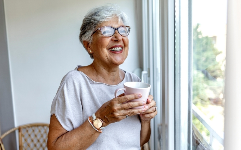 senior woman enjoying coffee at home looking out of window
